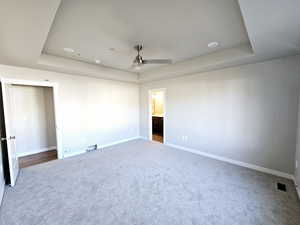 Carpeted empty room with visible vents, baseboards, a raised ceiling, and a ceiling fan