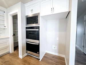 Kitchen with light wood-style floors, multiple ovens, stainless steel microwave, and white cabinets