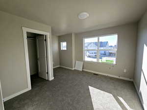 Unfurnished bedroom with visible vents, a spacious closet, baseboards, and dark carpet