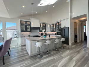 Kitchen featuring backsplash, a center island with sink, LVP floor, black appliances, and glass insert cabinets