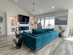 Living room with lofted ceiling, recessed lighting, light LVP flooring, and a glass covered fireplace