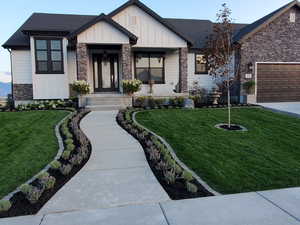 View of front facade with a shingled roof, stone siding, an attached garage, a front lawn, and board and batten siding