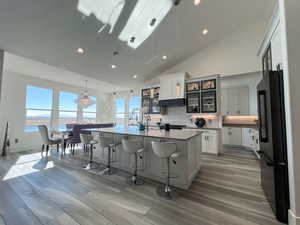 Kitchen with a center island with sink, decorative backsplash, glass insert cabinets, freestanding refrigerator, and a kitchen bar