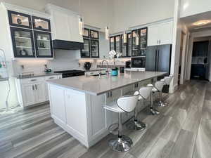 Kitchen with ventilation hood, a center island with sink, light LVP floors, and decorative backsplash