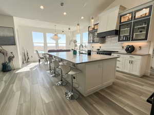 Kitchen with wood finish floors, a kitchen breakfast bar, white cabinets, decorative backsplash, and a center island with sink