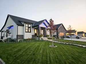 View of front of house with stone siding, a lawn, an attached garage, and concrete driveway