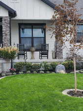 Doorway to property with covered porch, stone siding, board and batten siding, and a lawn