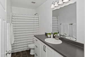 Full bathroom with toilet, curtained shower, visible vents, and vanity