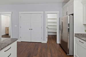 Kitchen featuring dark wood-type flooring, dark stone countertops, stainless steel fridge, and white cabinetry