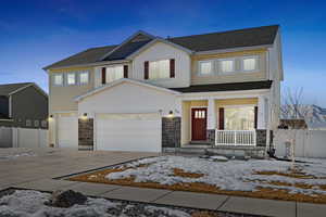 View of front of property featuring covered porch, an attached garage, fence, stone siding, and driveway