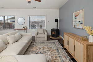 Living room featuring visible vents, a ceiling fan, baseboards, dark wood finished floors, and a wood stove