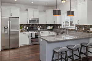 Kitchen with white cabinets, appliances with stainless steel finishes, a peninsula, light stone countertops, and a sink