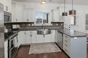 Kitchen with dark wood-style flooring, appliances with stainless steel finishes, white cabinetry, a sink, and a peninsula