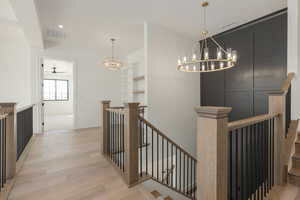 Corridor with light wood-type flooring, visible vents, a decorative wall, and an upstairs landing