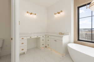 Bathroom featuring a sink, marble finish floor, a freestanding tub, and toilet