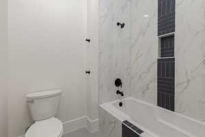 Full bathroom with toilet, tiled shower / bath combo, and baseboards