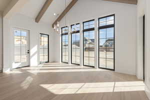 Spare room featuring a healthy amount of sunlight, light wood-style floors, high vaulted ceiling, and beam ceiling