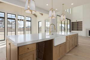 Kitchen with a center island with sink, light countertops, hanging light fixtures, light wood-style floors, and a sink