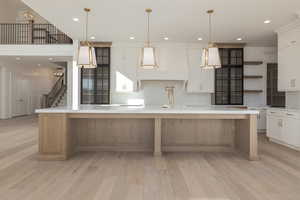 Kitchen with open shelves, light countertops, light wood-style floors, white cabinetry, and a large island with sink