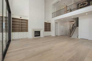 Unfurnished living room featuring a fireplace, light wood finished floors, stairway, a high ceiling, and an inviting chandelier