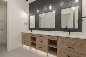 Bathroom featuring double vanity, wooden walls, baseboards, and a sink