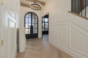 Foyer with stairway, a decorative wall, beamed ceiling, and a chandelier