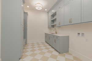 Kitchen featuring light floors, open shelves, gray cabinets, a sink, and baseboards