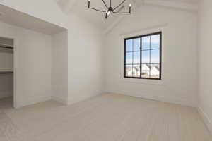 Interior space with a spacious closet, lofted ceiling with beams, an inviting chandelier, carpet flooring, and baseboards