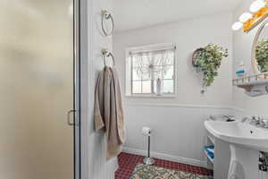 Bathroom featuring a sink, a shower stall, a textured ceiling, and wainscoting