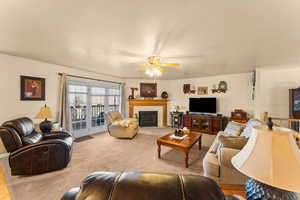 Living room featuring carpet, a fireplace with flush hearth, and ceiling fan