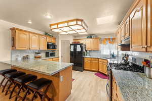 Kitchen with light wood-style flooring, under cabinet range hood, a peninsula, a skylight, and black appliances