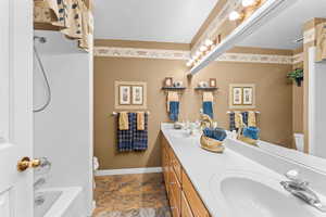 Full bathroom featuring toilet, double vanity, baseboards, and a sink