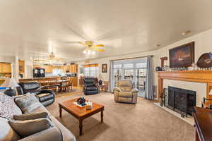 Living area with light carpet, a textured ceiling, a fireplace with flush hearth, and a ceiling fan