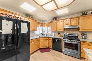 Kitchen featuring light wood-style flooring, under cabinet range hood, a sink, black appliances, and tasteful backsplash