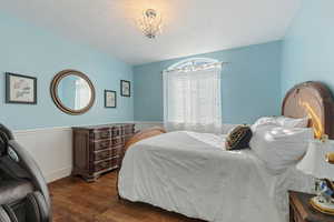 Bedroom with a chandelier, wood flooring, and a wainscoted wall