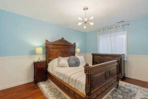 Bedroom with a chandelier, wainscoting, visible vents, and wood finished floors