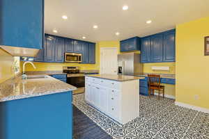 Kitchen with a center island, blue cabinets, stainless steel appliances, a sink, and recessed lighting