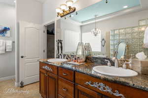 Bathroom featuring double vanity, a tray ceiling, a sink, and tile patterned floors