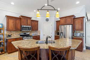 Kitchen featuring appliances with stainless steel finishes, a kitchen bar, a sink, and a kitchen island with sink