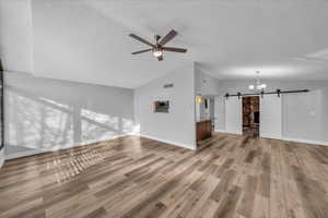 Unfurnished living room featuring lofted ceiling, a barn door, wood finished floors, and visible vents