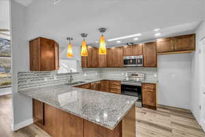 Kitchen with light wood-style flooring, stainless steel appliances, a peninsula, a sink, and brown cabinetry