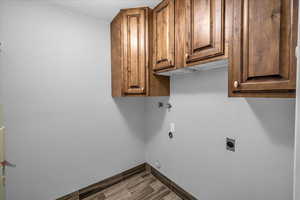 Washroom with hookup for a washing machine, cabinet space, hookup for an electric dryer, wood finished floors, and baseboards