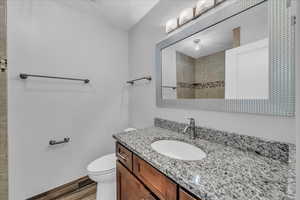 Full bathroom featuring vanity, wood finished floors, a tile shower, and toilet