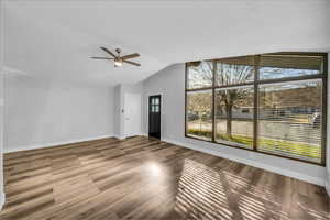 Unfurnished living room with lofted ceiling, a ceiling fan, baseboards, and wood finished floors