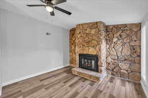 Unfurnished living room featuring a stone fireplace, wood finished floors, a ceiling fan, visible vents, and baseboards