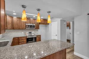 Kitchen with light stone counters, light wood finished floors, backsplash, appliances with stainless steel finishes, and a peninsula