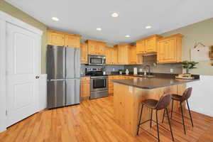 Kitchen with dark countertops, appliances with stainless steel finishes, light wood-style floors, a sink, and a peninsula