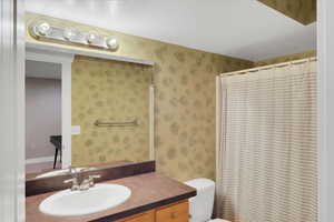 Bathroom featuring curtained shower, toilet, a textured ceiling, vanity, and wallpapered walls