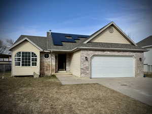 Ranch-style home with a garage, concrete driveway, a shingled roof, and roof mounted solar panels