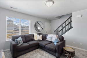 Living room featuring carpet floors, stairway, visible vents, and baseboards